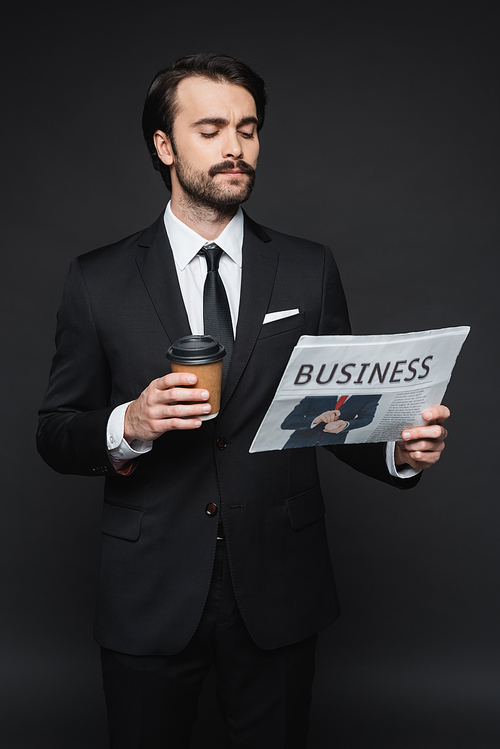 man with mustache holding paper cup and reading business newspaper on dark grey