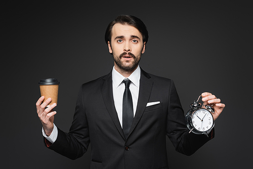 businessman with mustache holding paper cup and alarm clock on dark grey