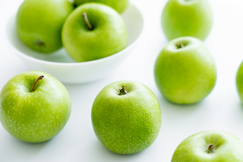 green and ripe apples near bowl on white