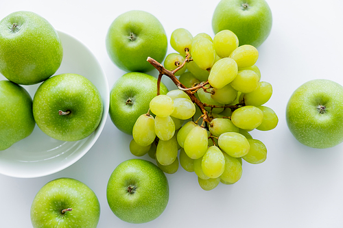 top view of green and ripe apples in bowl near grapes on white