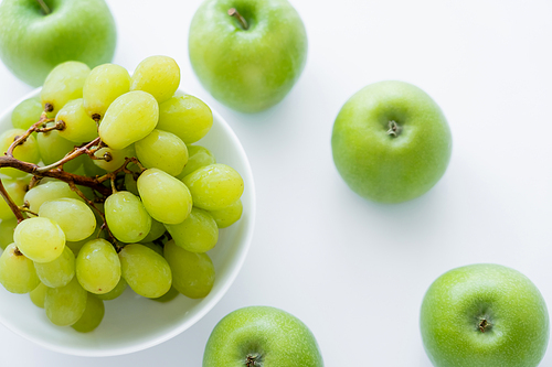 top view of green apples near grapes in bowl on white