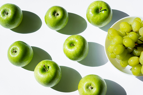 top view of ripe apples near tasty grapes in bowl on white