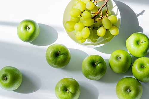 top view of bowl with sweet grapes and apples on white