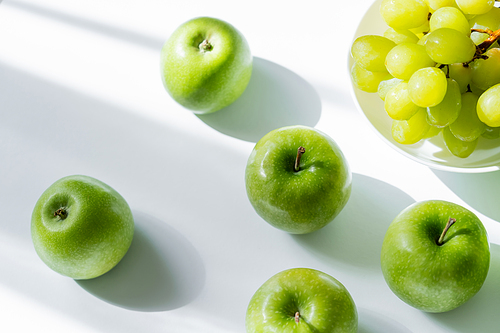 top view of bowl with sweet grapes and ripe apples on white