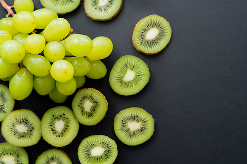 top view of green ripe grapes and sliced kiwi on black