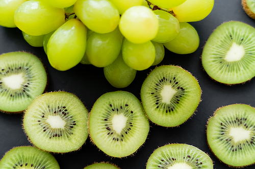 top view of green grapes and sliced fresh kiwi on black