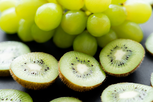 close up view of green grapes and sliced fresh kiwi on black