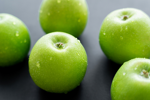 close up view of water drops on green and ripe apples on black