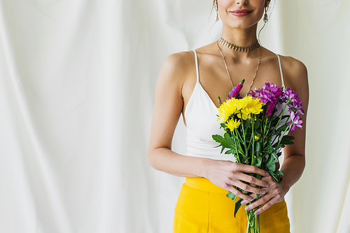 cropped view of happy woman in crop top holding flowers on white