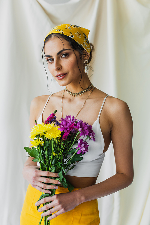 brunette woman in yellow headscarf holding flowers on white
