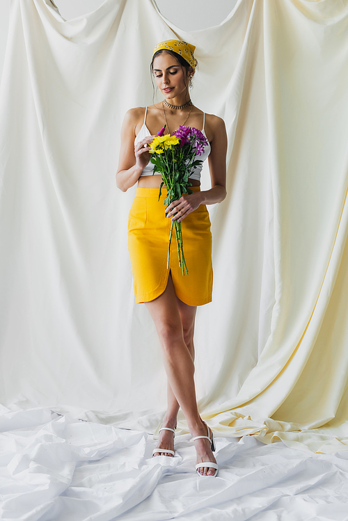 full length of woman in yellow headscarf holding flowers on white