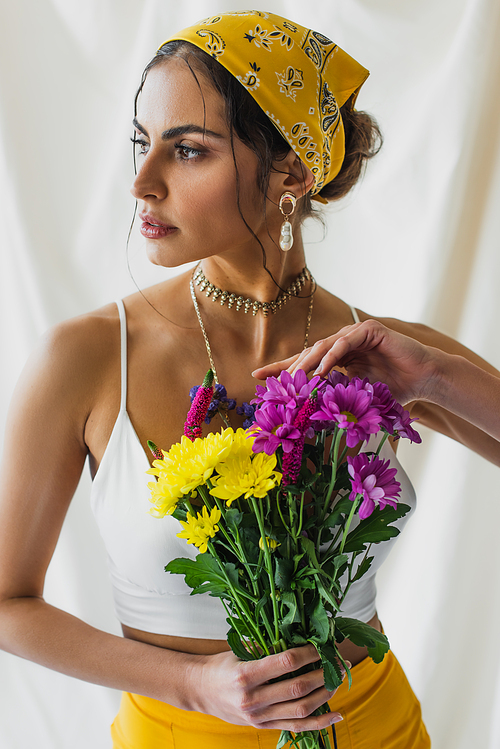 woman in yellow headscarf holding bouquet of flowers on white