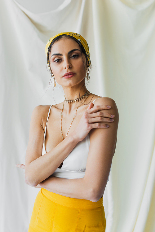woman in yellow headscarf and crop top posing on white