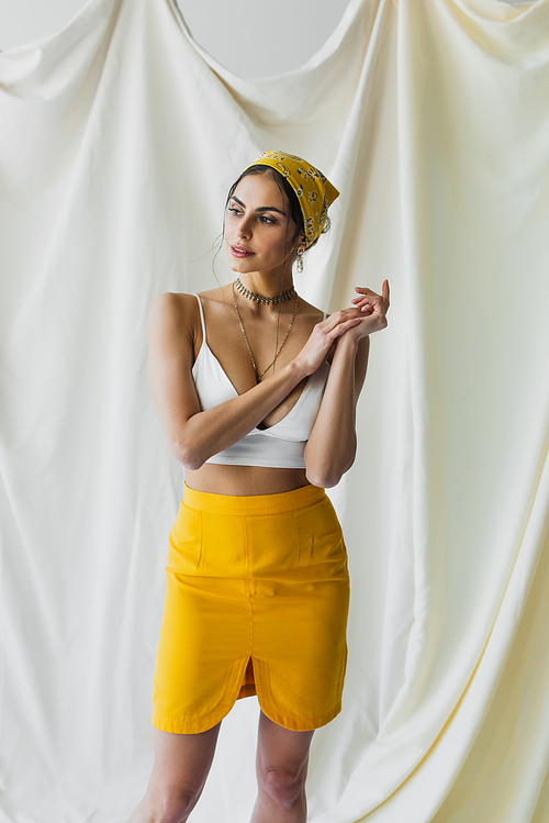 stylish woman in yellow headscarf, skirt and crop top posing on white