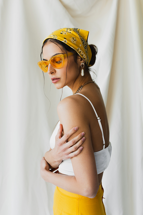 woman in yellow sunglasses and headscarf posing on white