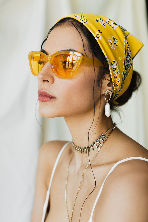 stylish woman in trendy sunglasses and yellow headscarf posing on white