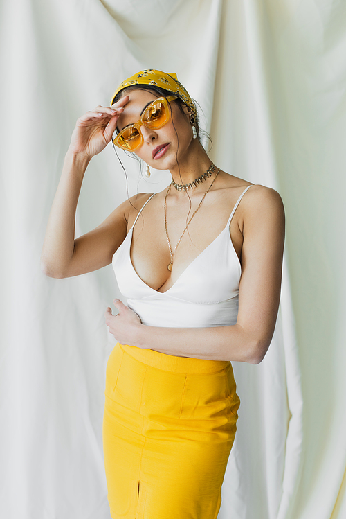 stylish woman in sunglasses and yellow headscarf posing on white