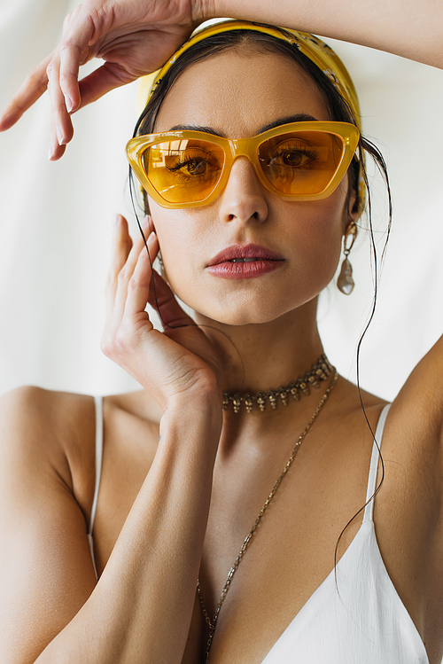 pretty woman in stylish sunglasses and yellow headscarf posing on white