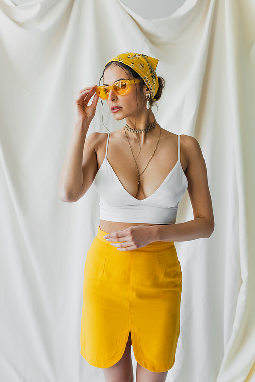 stylish woman adjusting sunglasses and posing on white
