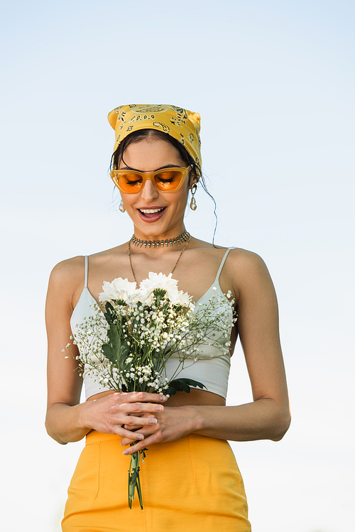 amazed woman in sunglasses and yellow headscarf looking at flowers