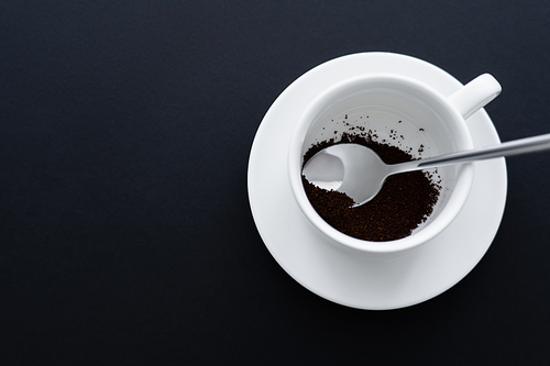 top view of ground coffee in cup with spoon on black