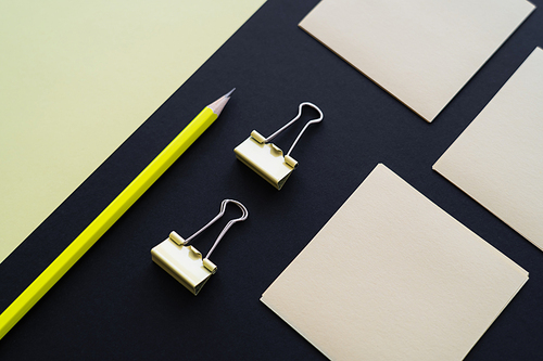 flat lay of blank paper near sticky notes, pencil and fold back clips on black