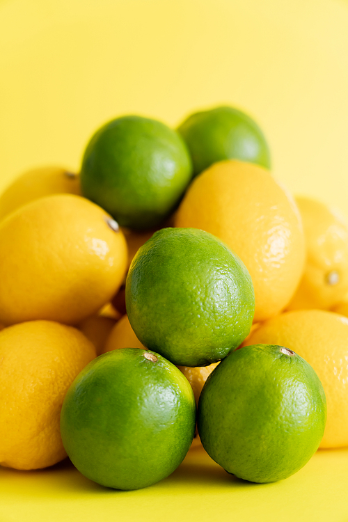 Close up view of organic limes near blurred lemons on yellow surface