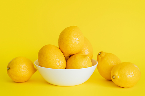 Fresh lemons in bowl and on yellow surface