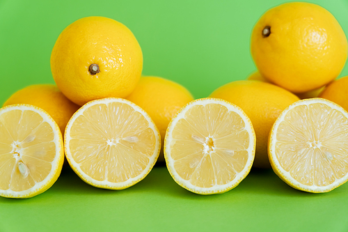 Bright halves and whole lemons on green background