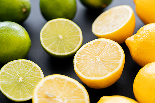 Close up view of bright lemons and limes near blurred fruits on black background
