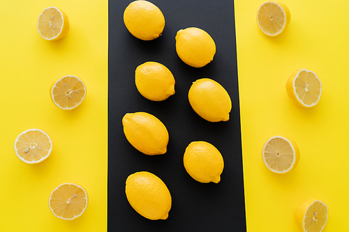 Flat lay with ripe whole and cup lemons on black and yellow background