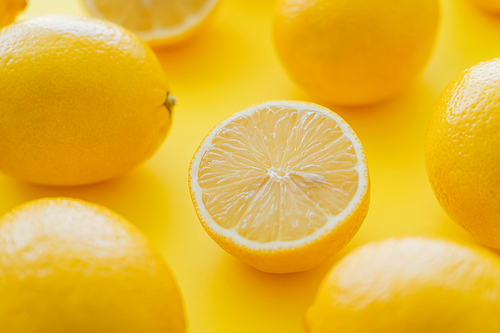 Close up view of cut and blurred whole lemons on yellow surface