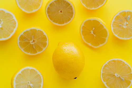 Top view of whole and halves of organic lemons on yellow surface
