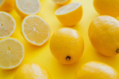 Close up view of fresh lemons near blurred halves on yellow surface