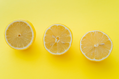 Top view of fresh halves of lemons on yellow surface