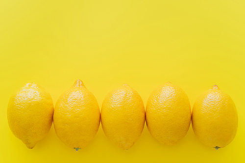 Top view of row of lemons on yellow surface with copy space