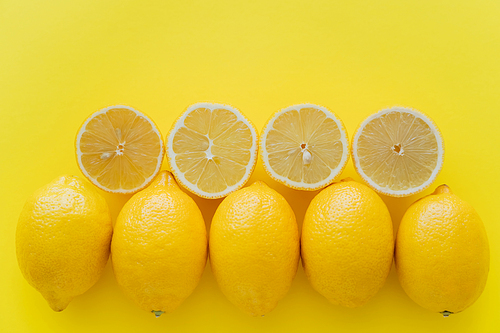 Top view of rows of whole and cut lemons on yellow surface