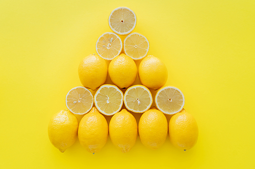 Flat lay with whole and cut lemons in triangle shape on yellow surface