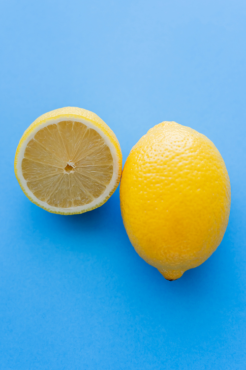 Close up view of cut and whole bright lemons on blue background