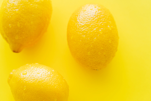 Top view of wet lemons on yellow background