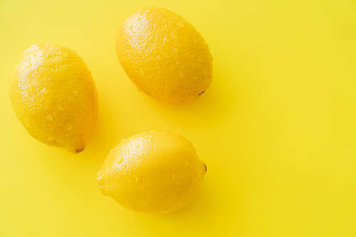 Top view of ripe lemons with wet peel on yellow surface