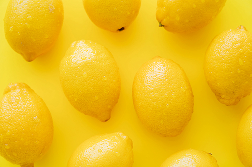 Top view of fresh lemons with droplets on peel on yellow surface