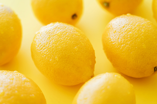Close up view of organic and wet lemons on yellow surface