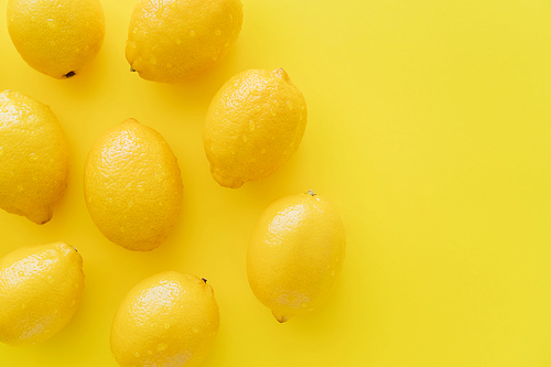 Top view of ripe lemons with water drops on peel on yellow surface