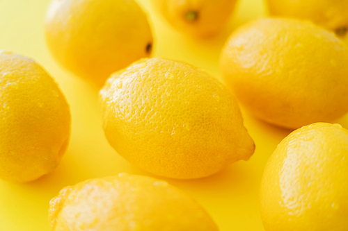Close up view of wet lemons on yellow surface