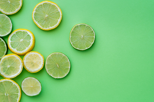 Top view of sliced fresh lemons and limes on green background with copy space