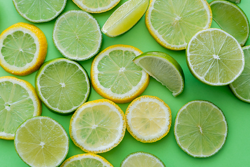 Top view of sliced and cut lemons and limes on green background