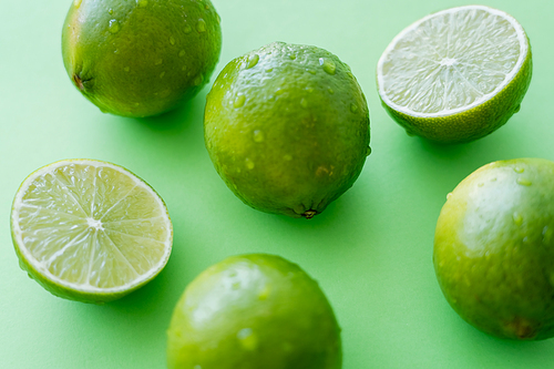 Close up view of ripe limes with water drops on green background