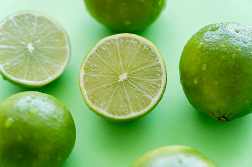 Close up view of juicy limes with water drops on green background