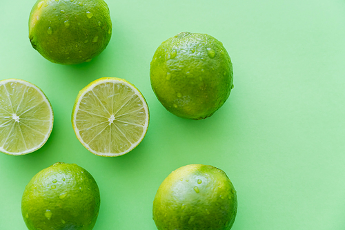 Top view of whole and cut limes with water drops on green background